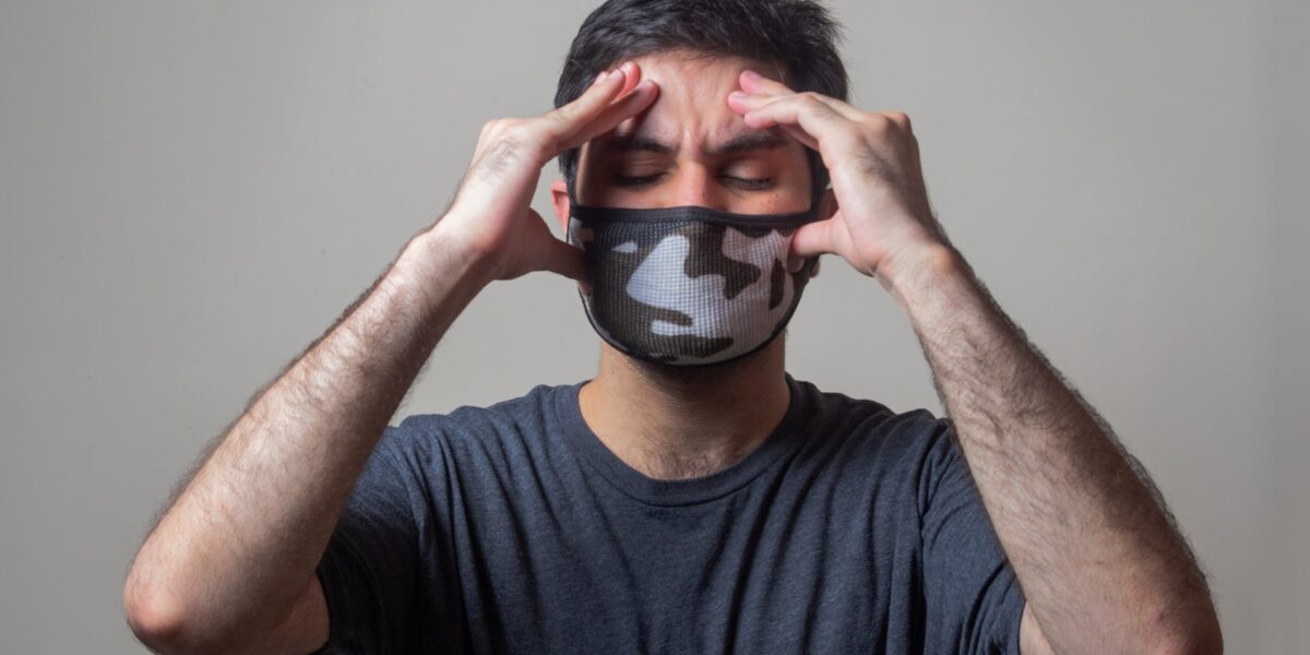 Homem com máscara no rosto e mãos na cabeça